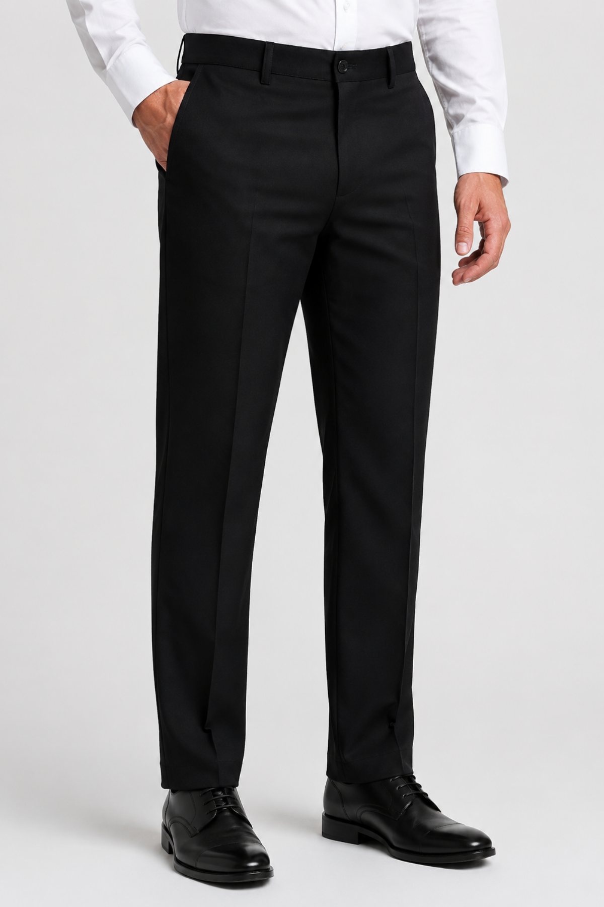 A man wearing black dress pants with a white dress shirt and black leather dress shoes, shown from the waist down against a light gray studio background.